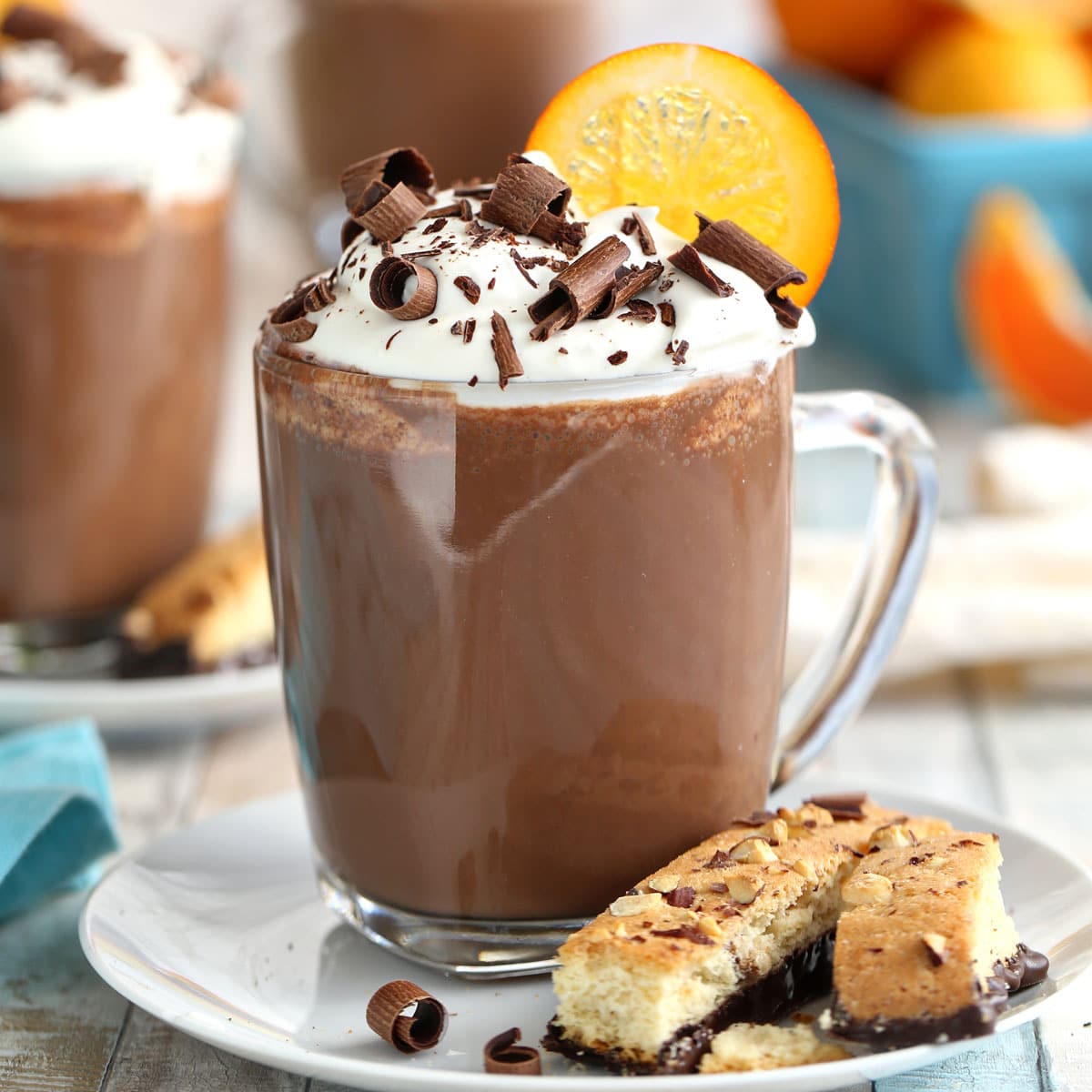 A cup of Orange Hot Chocolate on a small white plate next to biscotti.