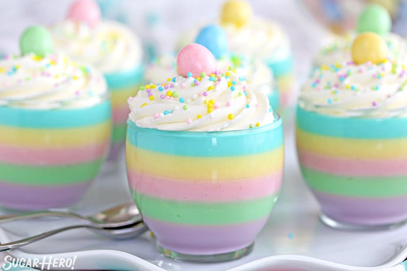Four pastel rainbow gelatin cups topped with candy eggs and sprinkles.