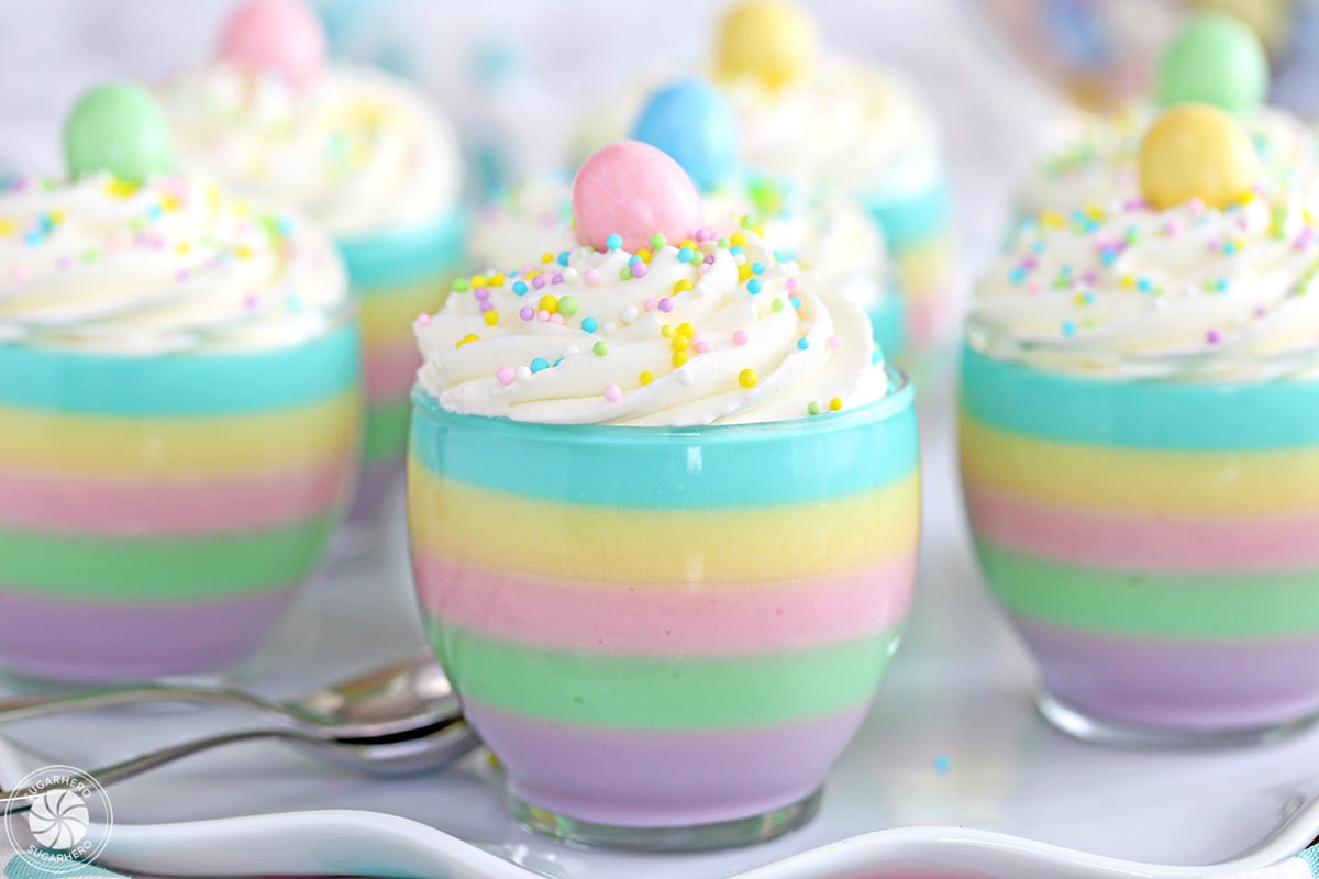 Four pastel rainbow gelatin cups topped with candy eggs and sprinkles.