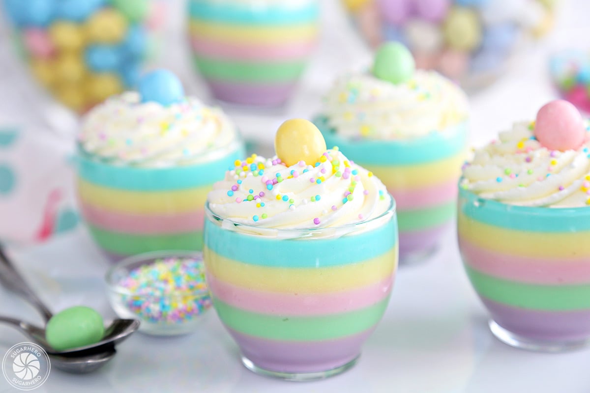 A group of striped pastel gelatin cups all arranged together, with whipped cream swirls on top.