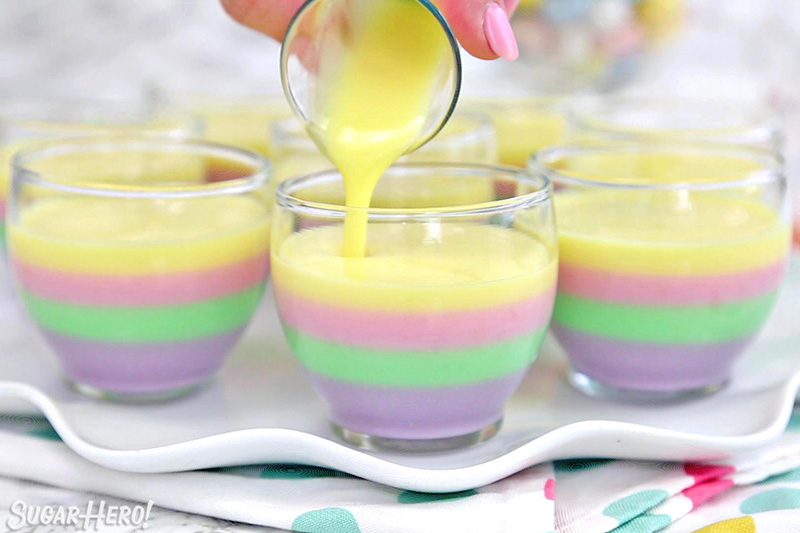 Pouring yellow gelatin on top of pink, green, and purple layers for pastel rainbow gelatin cups.