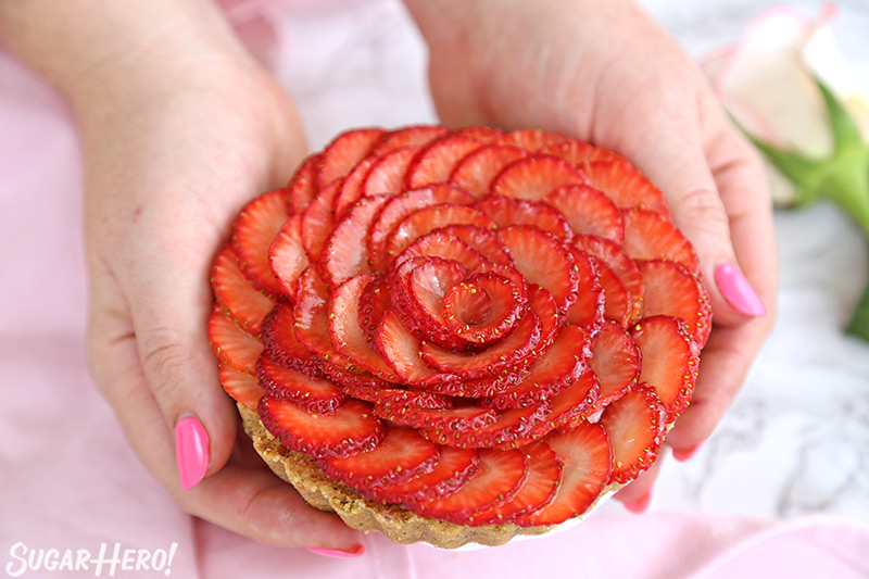 Hands with pink fingernails holding a miniature Strawberry Rose Tart.