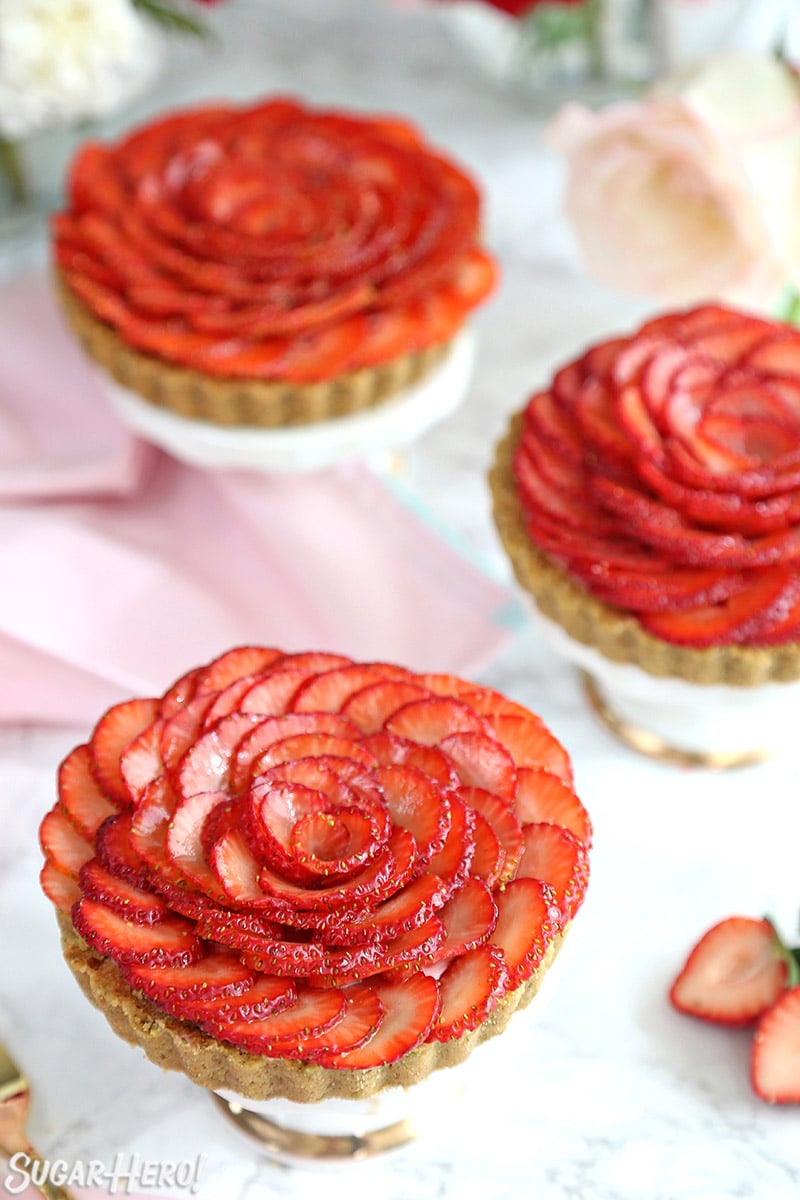 Three Strawberry Rose Tarts on mini cake stands with a pink napkin behind them.