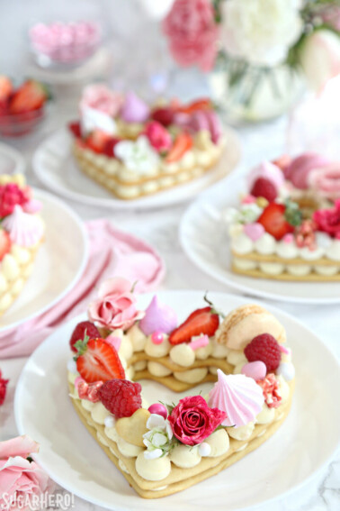 Four trendy cream tarts topped with berries and various candies on a white round plate.