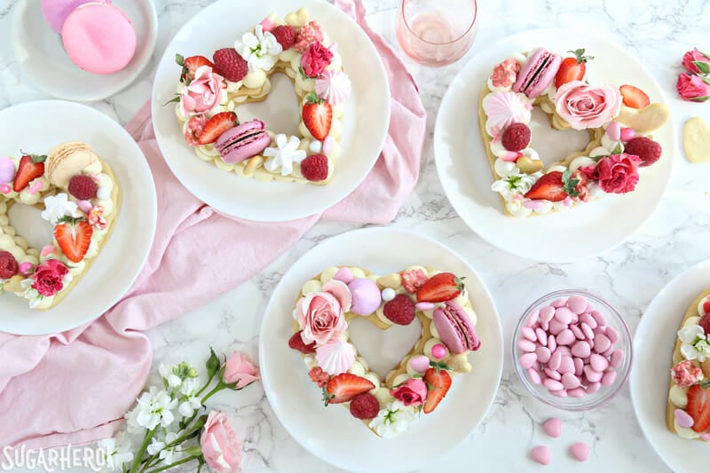 Trendy Cream Tarts - overhead shot of five heart-shaped cream biscuits with flowers, berries, and candy on top | From SugarHero.com