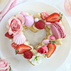 Close up of trendy cream tart topped with berries and assorted candies on a round white plate.