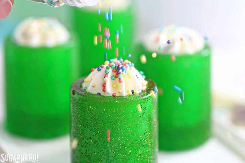 DIY Candy Shot Glasses - now you can make your own edible shot glasses out of sugar! Fill them with your favorite drink, whipped cream, mousse, or whatever else you'd like! | From SugarHero.com DIY Candy Shot Glasses - pouring sprinkles on top of whipped cream in a candy shot glass | From SugarHero.com