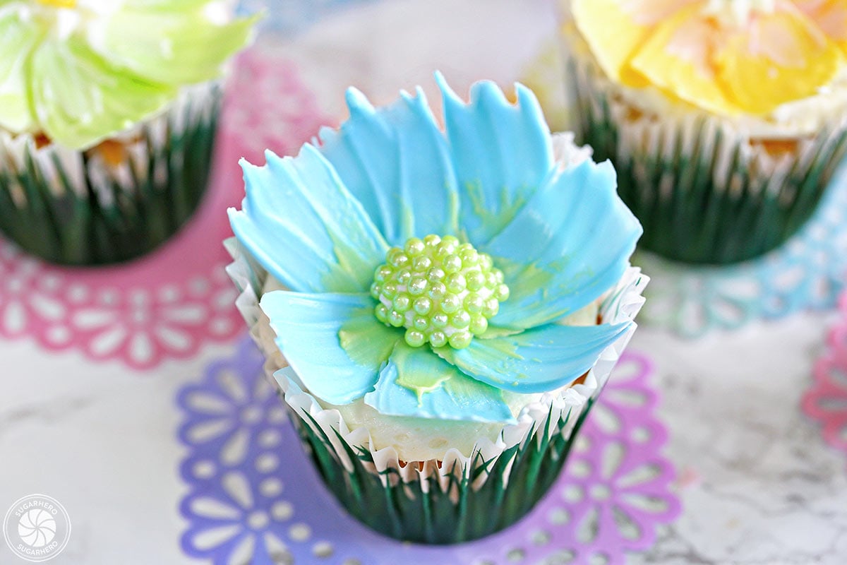 Three chocolate flower cupcakes sitting on colorful doilies.