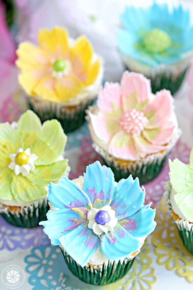 Six chocolate flower cupcakes sitting on colorful doilies.
