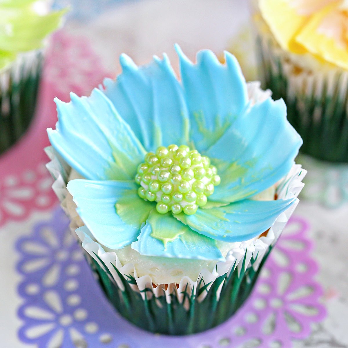 Close up of a blue chocolate flower cupcake sitting on a pink and purple doily.