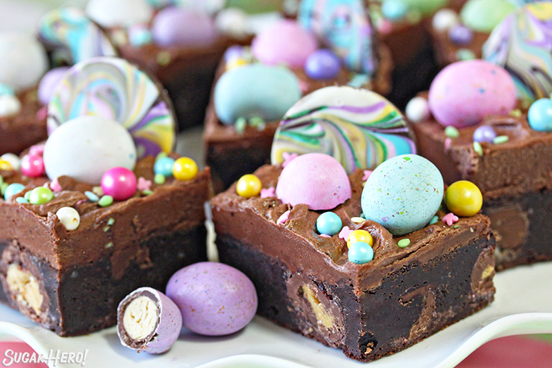 Eight Easter Egg Brownies covered in chocolate frosting and topped with chocolate eggs and sprinkles.