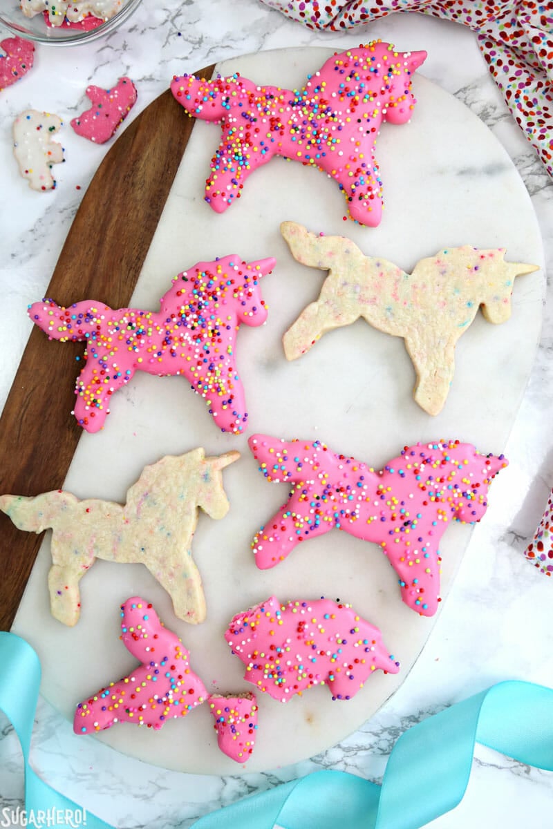 Circus Animal Layer Cake - a big, bright pink cake with funfetti cake layers, chopped up circus animal cookies inside, and a cool upside-down ganache drip decoration! | From SugarHero.com Circus Animal Layer Cake - funfetti unicorn sugar cookies on a platter, some dipped in pink coating and some left plain | From SugarHero.com