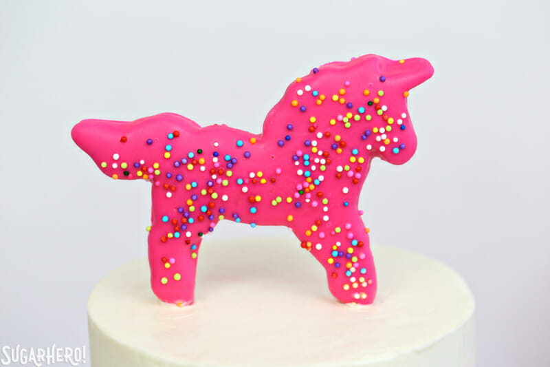 Circus Animal Layer Cake - close-up of pink sprinkled unicorn cookie on top of circus animal cake | From SugarHero.com