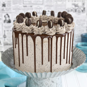 Cookies and cream cake on a silver cake stand on a white surface with a blue cloth.