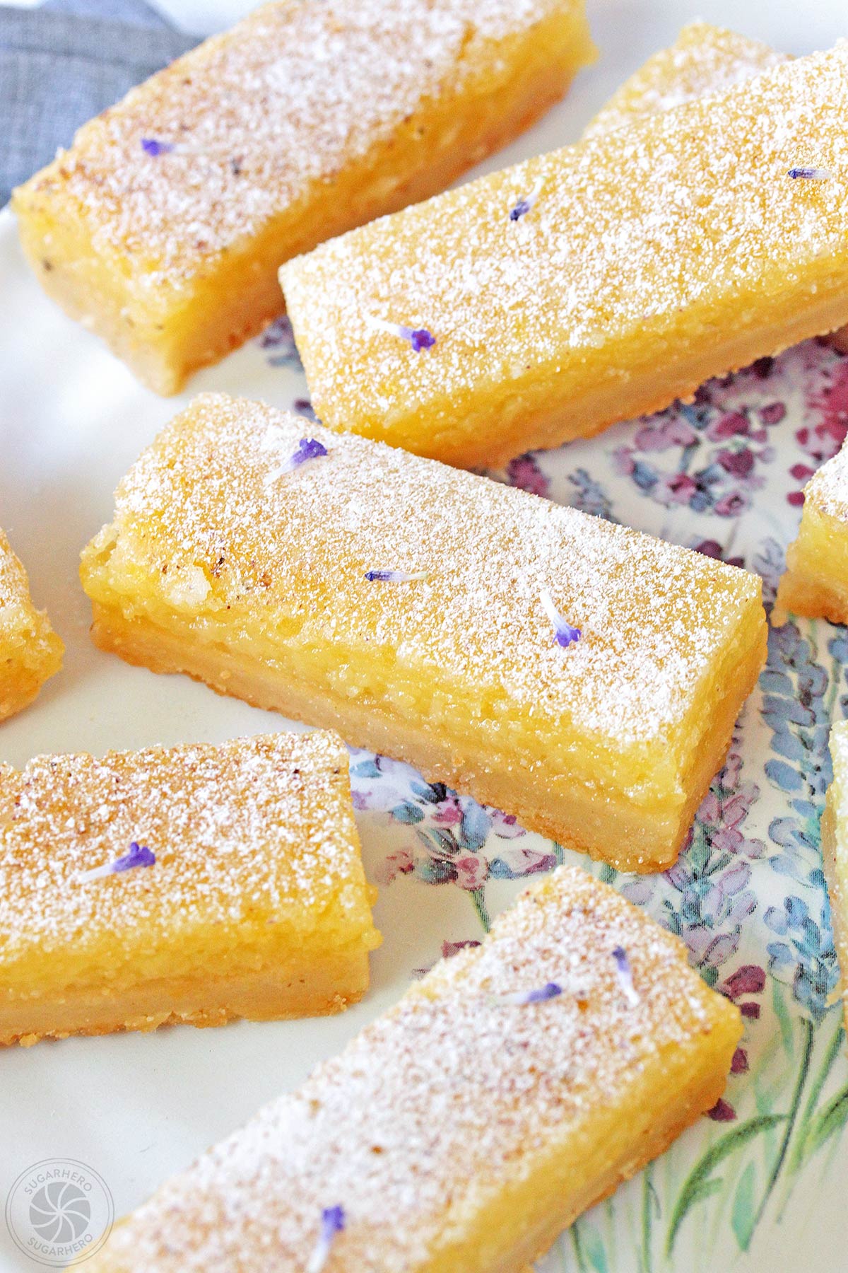 Like lemon bars? Then you'll love this spring twist on the classic--tangy lemon bars with a light lavender flavor! Easy and delicious! | From SugarHero.com Lavender Lemon Bars - close-up of lemon bars with powdered sugar and lavender buds sprinkled on top | From SugarHero.com