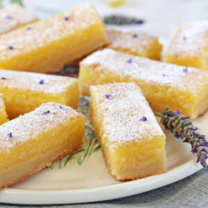 Ten lavender lemon bars on a white round plate with a lavender flower on it.