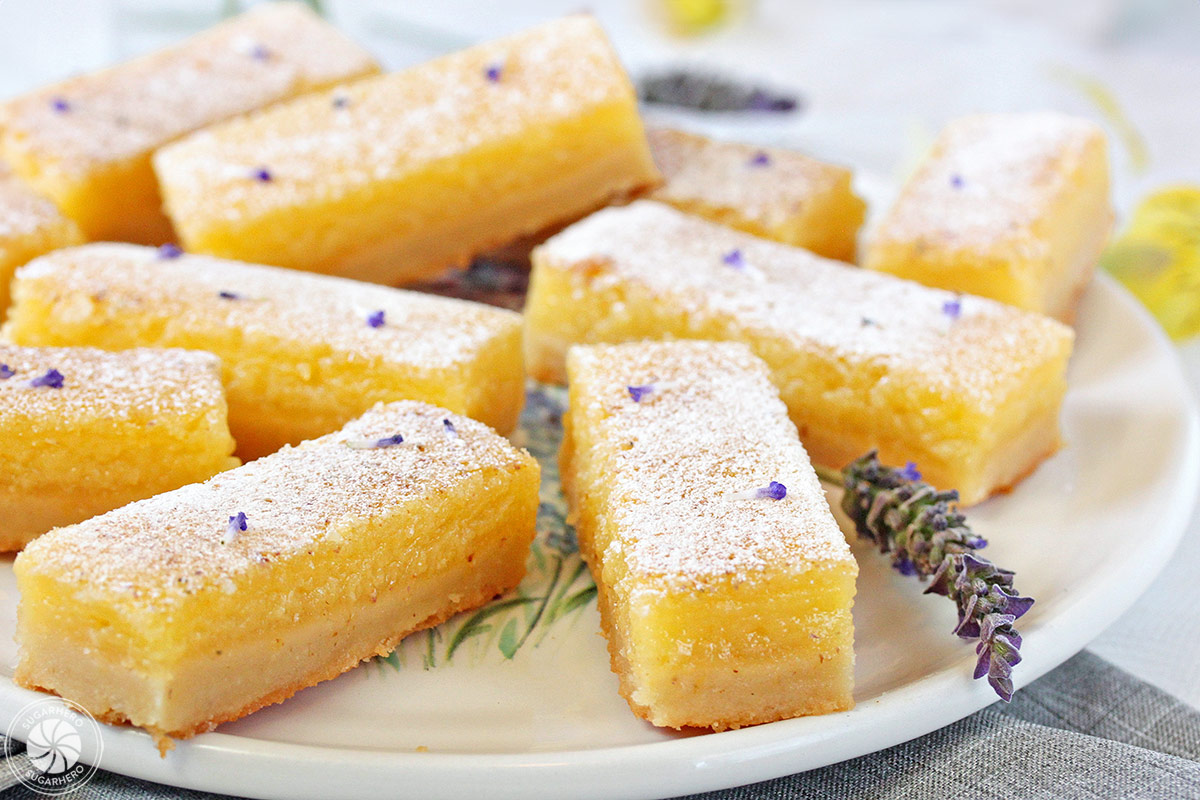 Like lemon bars? Then you'll love this spring twist on the classic--tangy lemon bars with a light lavender flavor! Easy and delicious! | From SugarHero.com Lavender Lemon Bars - rectangular bars arranged on a plate | From SugarHero.com