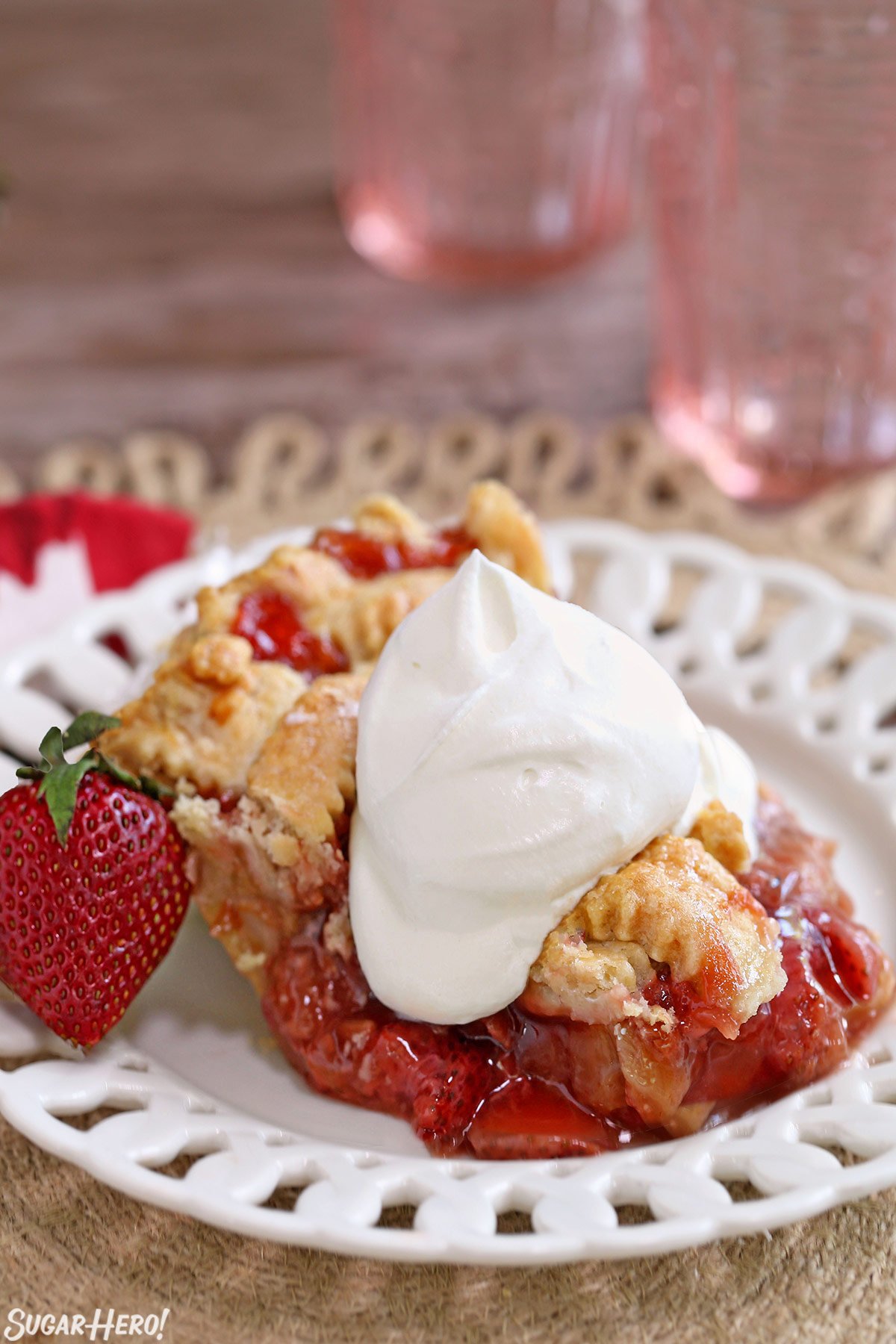 Strawberry Rhubarb Pie is a summertime classic! A flaky, buttery crust is filled with the perfect combination of sweet, juicy strawberries and tart rhubarb. | From SugarHero.com Strawberry Rhubarb Pie - single slice on a plate with whipped cream on top | From SugarHero.com