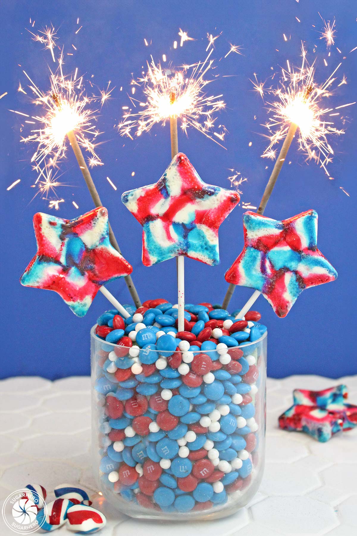 Easy Homemade Lollipops - swirled red, white, and blue lollipops with sparklers behind them | From SugarHero.com