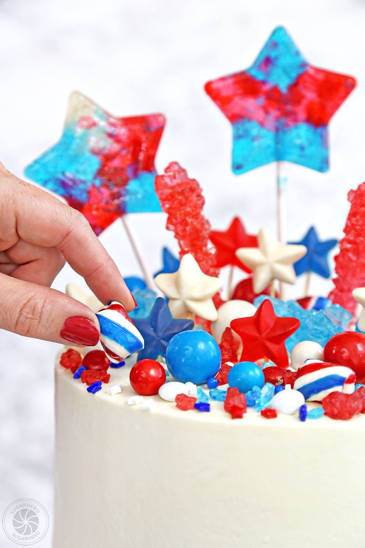 Fourth of July Layer Cake - hand placing mint twist candy on top of cake | From SugarHero.com 