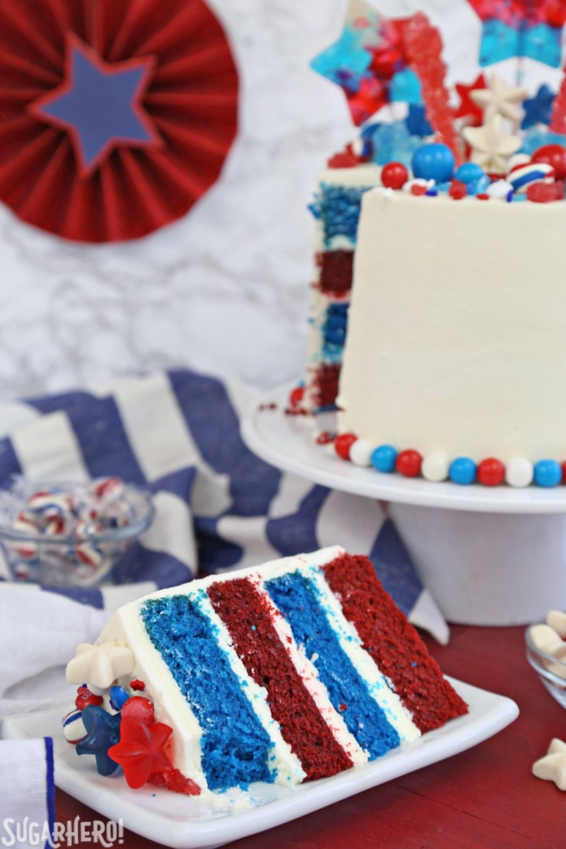 Fourth of July Layer Cake - slice of red and blue velvet cake displayed in front of a tall layer cake | From SugarHero.com 