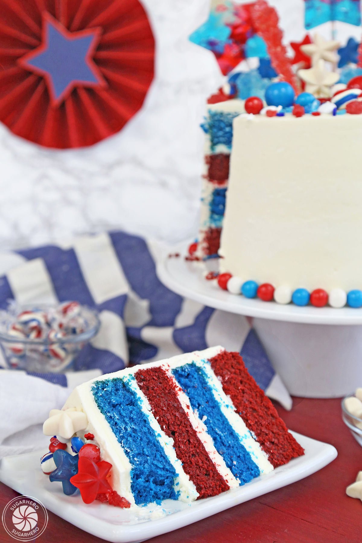 Fourth of July Layer Cake - slice of red and blue velvet cake displayed in front of a tall layer cake | From SugarHero.com 