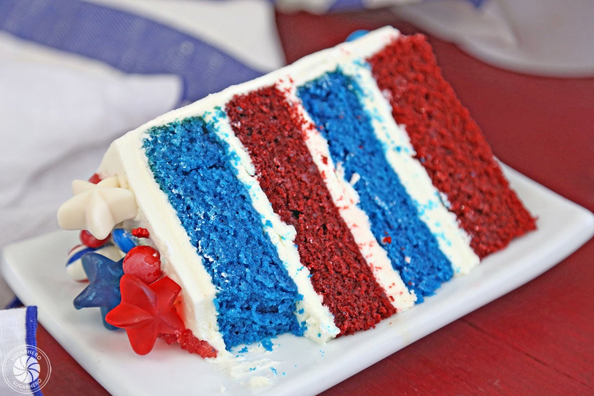 Fourth of July Layer Cake - close-up of slice of red and blue velvet cake with a bite taken out of it | From SugarHero.com 