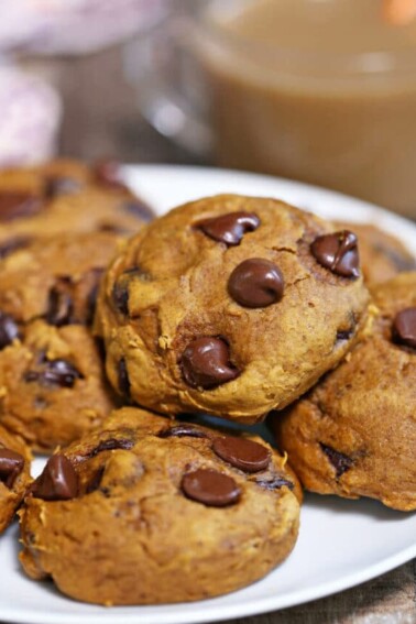 several baked chocolate chip cookies on a white plate with hot beverage in the background