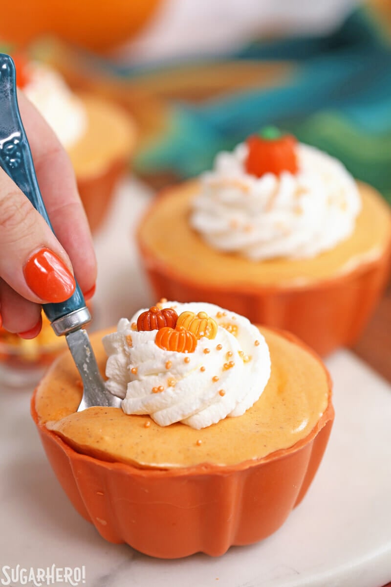 Pumpkin Spice Mousse Cups - This light and fluffy mousse is packed with fall flavor and made with real pumpkin, for an authentic pumpkin spice taste. It’s served in a cute edible candy bowl too! | From SugarHero.com Pumpkin Spice Mousse Cups - hand taking a spoonful of pumpkin spice mousse from the mousse cup | From SugarHero.com