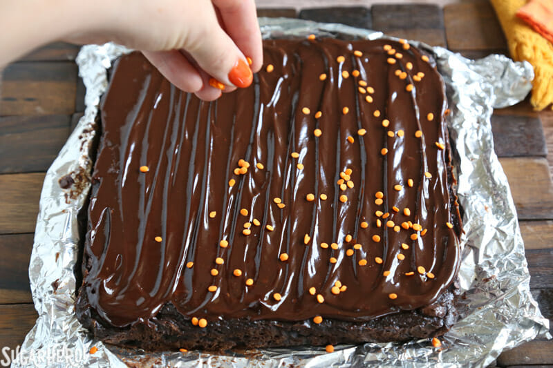 2-Ingredient Pumpkin Brownies - adding orange sprinkles on top of shiny chocolate glaze | From SugarHero.com