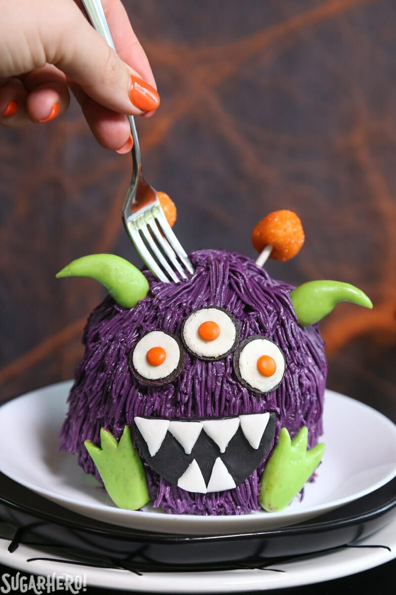 Monster Cake - This cute Halloween layer cake has a base covered in sprinkles, and a top layer decorated to look like a mini monster. Perfect for parties and spooky occasions! | From SugarHero.com Mini monster cake on a plate with a fork digging into the top of the cake