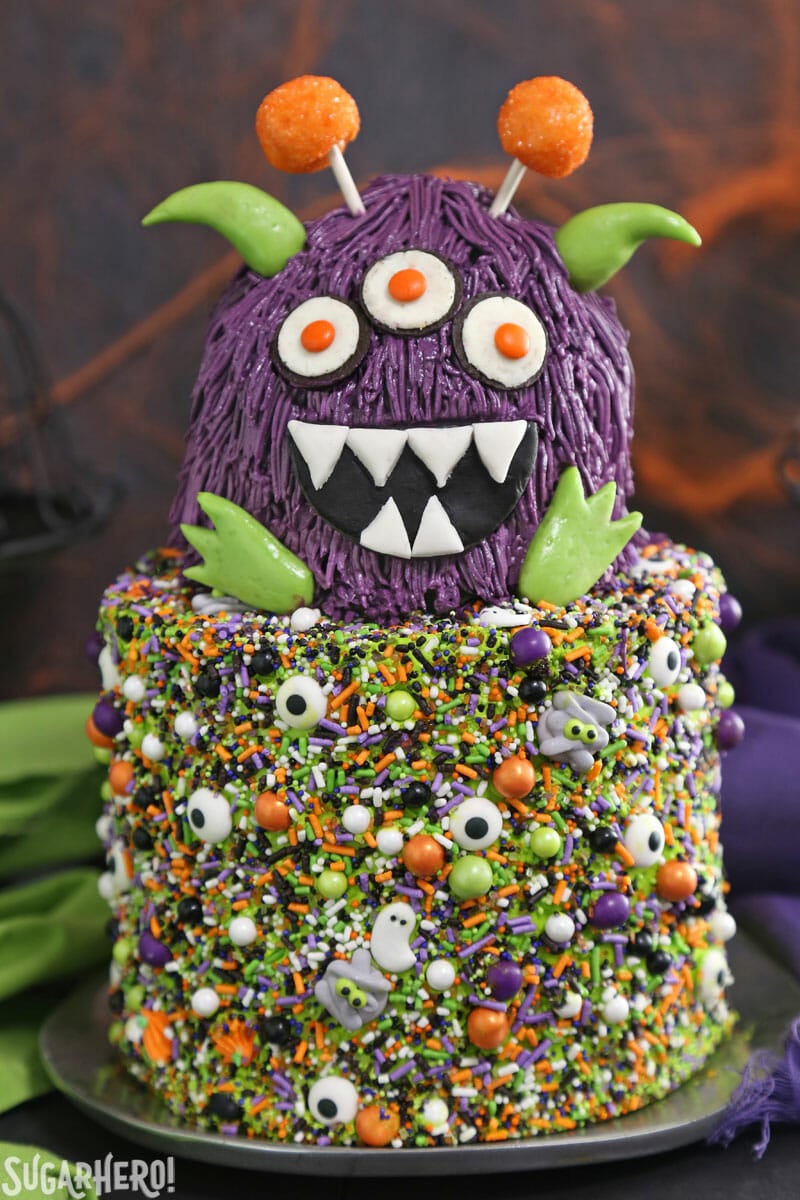 Monster Cake - This cute Halloween layer cake has a base covered in sprinkles, and a top layer decorated to look like a mini monster. Perfect for parties and spooky occasions! | From SugarHero.com Two-layer Monster Cake with fondant decorations and sprinkles on the bottom