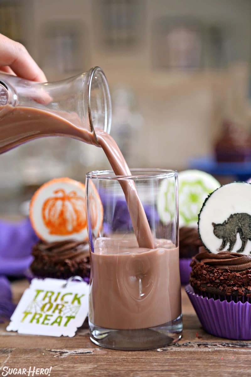 Stamped Halloween Cupcakes - These cute, customized stamped fondant toppers are SO EASY to make! Put them on double chocolate cupcakes for a delicious Halloween treat! | From SugarHero.com Stamped Halloween Cupcakes - pouring chocolate milk into a glass with chocolate cupcakes nearby | From SugarHero.com