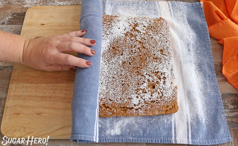 a shot of the pumpkin roll being rolled into a cotton towel. 