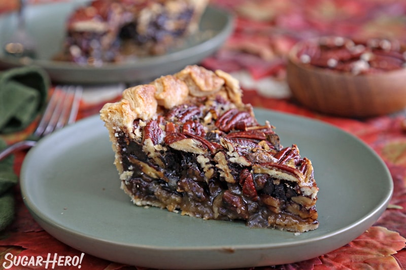 Deep Dish Pecan Pie - one slice of pecan pie on a green plate with a bowl of pecans in the background | From SugarHero.com