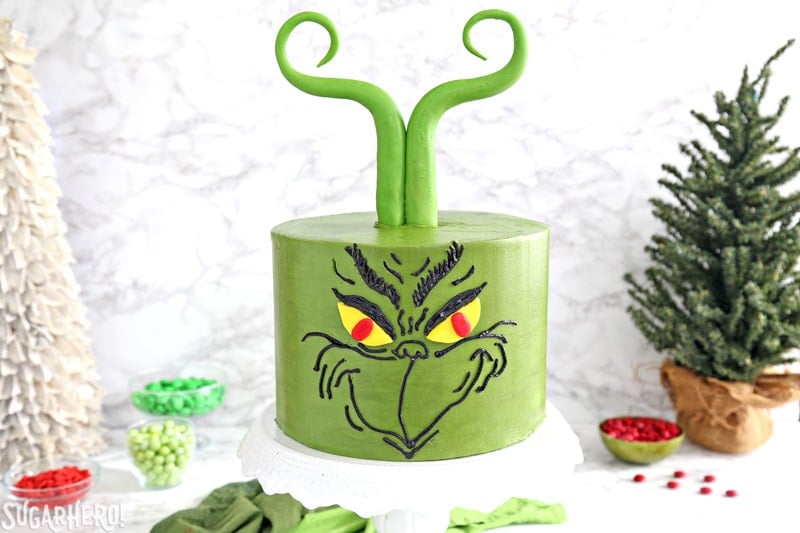 Grinch Cake - green cake with a Grinch face piped in black buttercream, and green Grinch fondant hair | From SugarHero.com