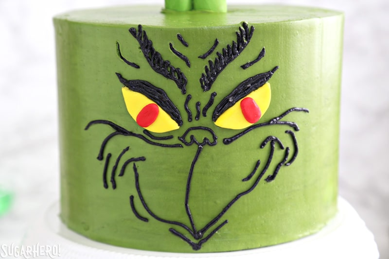 Grinch Cake - close-up of the Grinch's face, done in black buttercream on a green cake | From SugarHero.com