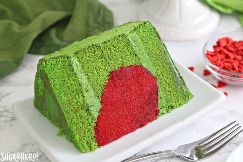 Grinch Cake - close-up of one slice of Grinch cake, made from green cake layers and a bright red heart inside | From SugarHero.com