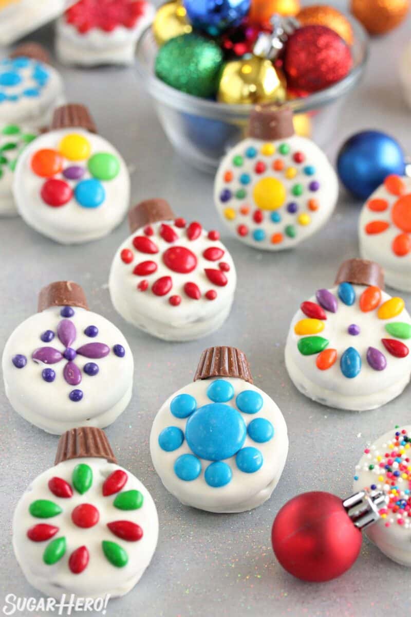 These cute Oreo Cookie Christmas Ornaments are a quick and easy holiday treat! They're a simple Christmas cookie even kids can help make. | From SugarHero.com Oreo Cookie Christmas Ornaments on a glittery background with colorful ornaments scattered around.
