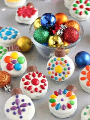 Oreo Cookie Christmas Ornaments on a glittery background with colorful ornaments in a bowl behind them.