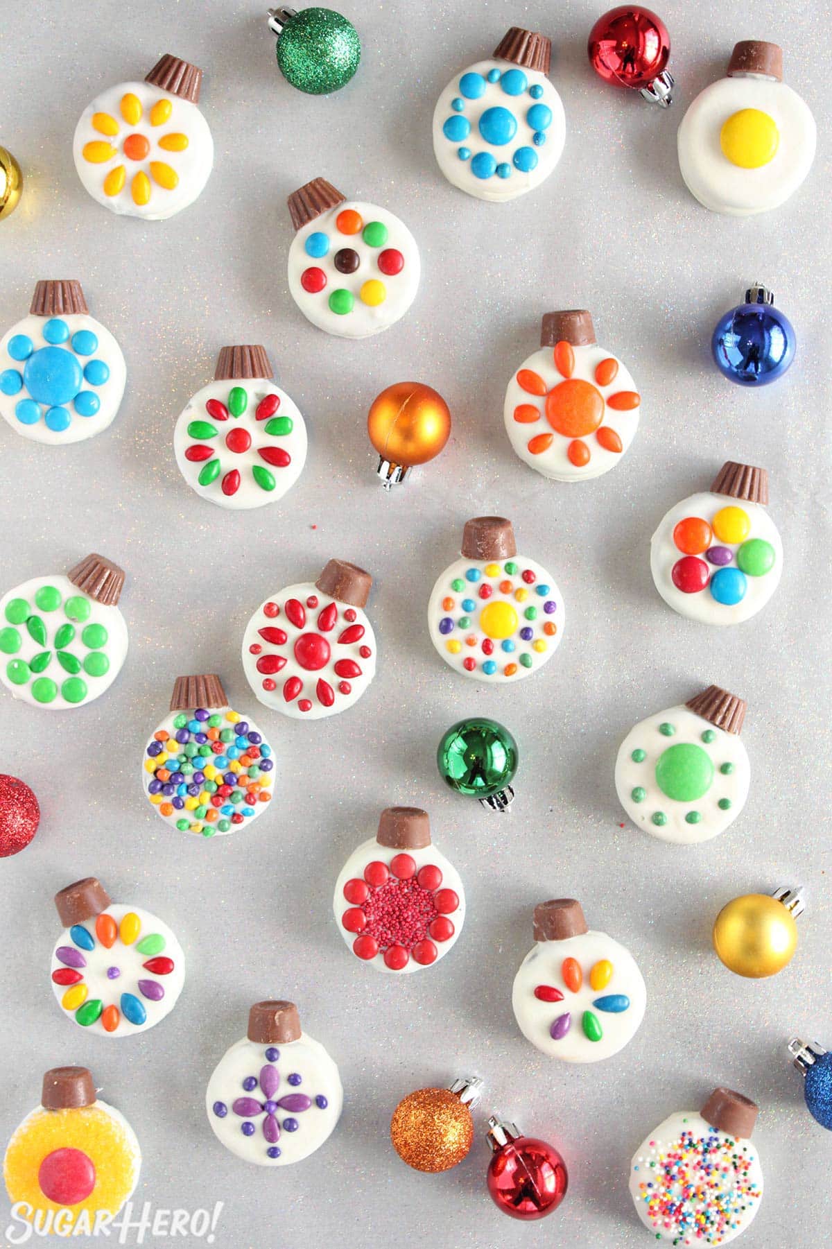 Overhead shot of colorful Oreo Cookie Christmas Ornaments on a silver background with colorful ornaments around.