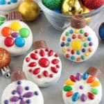 Oreo Cookie Christmas Ornaments on a glittery background with colorful ornaments in a bowl behind them.