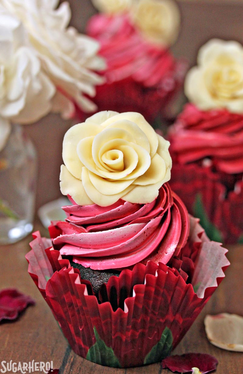 Chocolate Rose Cupcakes are moist chocolate cupcakes, topped with a beautiful swirl of red frosting and a sweet white chocolate rose. Learn how to make these hand-formed edible roses, and use them on cupcakes, cakes, and so many more desserts! | From SugarHero.com Chocolate Rose Cupcakes - A single chocolate cupcake with a white chocolate rose on top. | From SugarHero.com