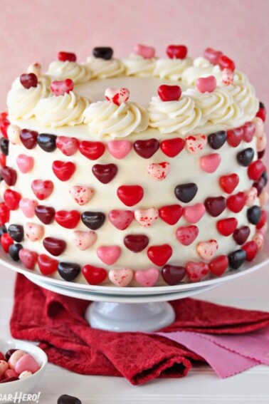 Pink and red velvet cake on a white cake stand, decorated with jelly bean hearts.
