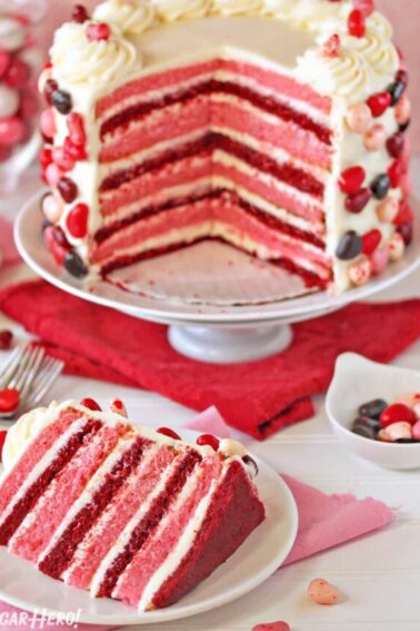 Pink and red velvet layer cake with several slices taken out, and a slice of cake displayed in front on a white plate.