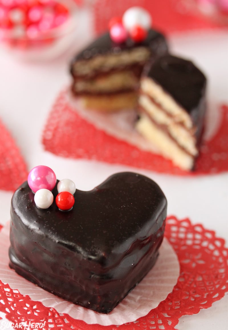 Nutella Pound Cake Petit Fours have big flavor in a small package! These sweet heart-shaped desserts are perfect for Valentine's Day or any special occasion. | From SugarHero.com Nutella Pound Cake Petit Fours - A petit four covered in a chocolate glaze with pink and red candy on top. | From SugarHero.com