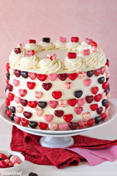 Pink and red velvet cake on a white cake stand, decorated with jelly bean hearts.