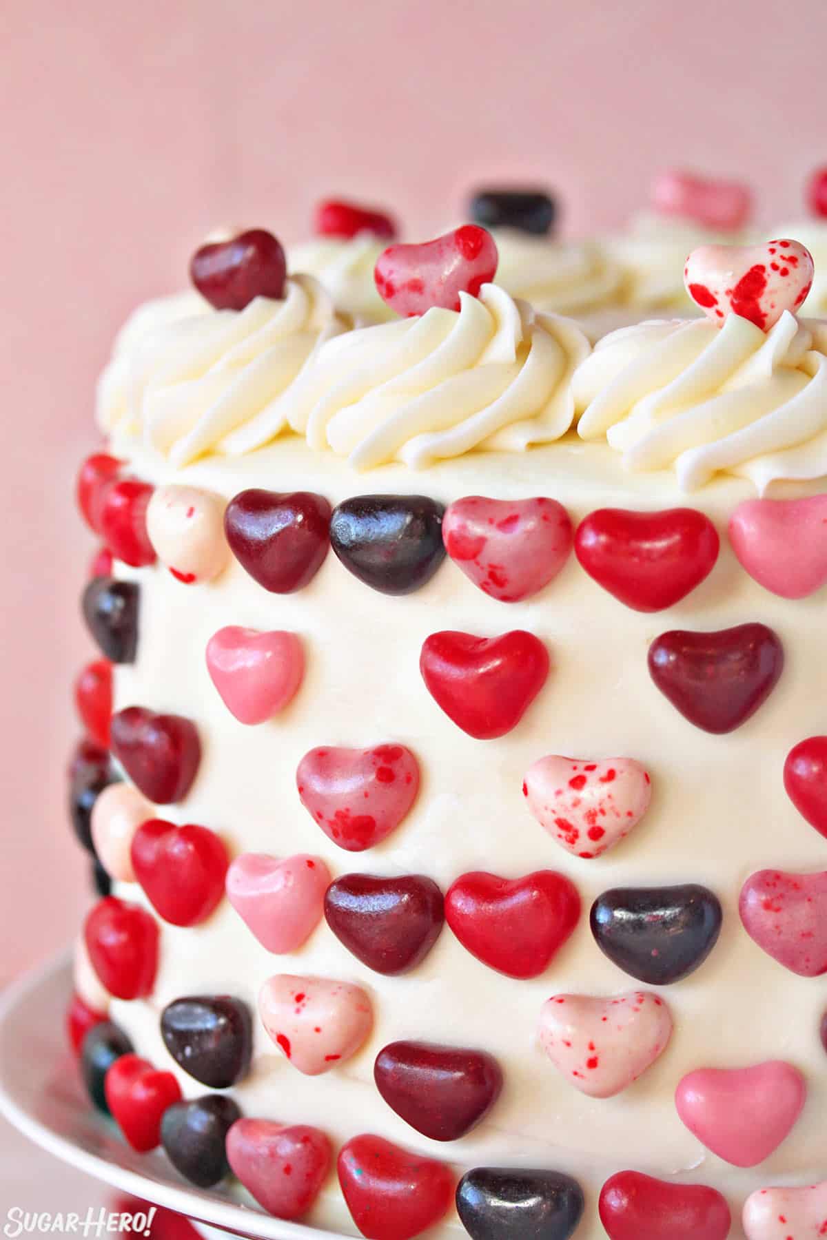 Close-up of the side of a cake, showing the cream cheese frosting and red and pink candy decorations.