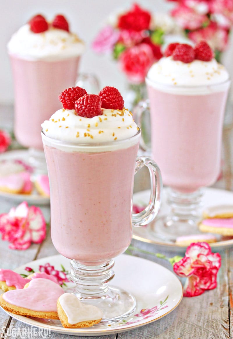 Raspberry White Hot Chocolate is a pretty pink twist on traditional hot chocolate! It's made with white chocolate and real raspberry puree, for a fresh, fruity taste that is perfect year-round! | From SugarHero.com Raspberry White Hot Chocolate - Three separate glasses with hot chocolate and raspberries on top | From SugarHero.com