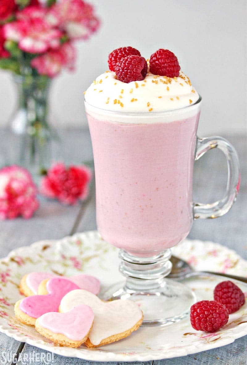 Raspberry White Hot Chocolate - A single cup of hot chocolate with raspberries on top and heart shaped cookies to the side | From SugarHero.com 